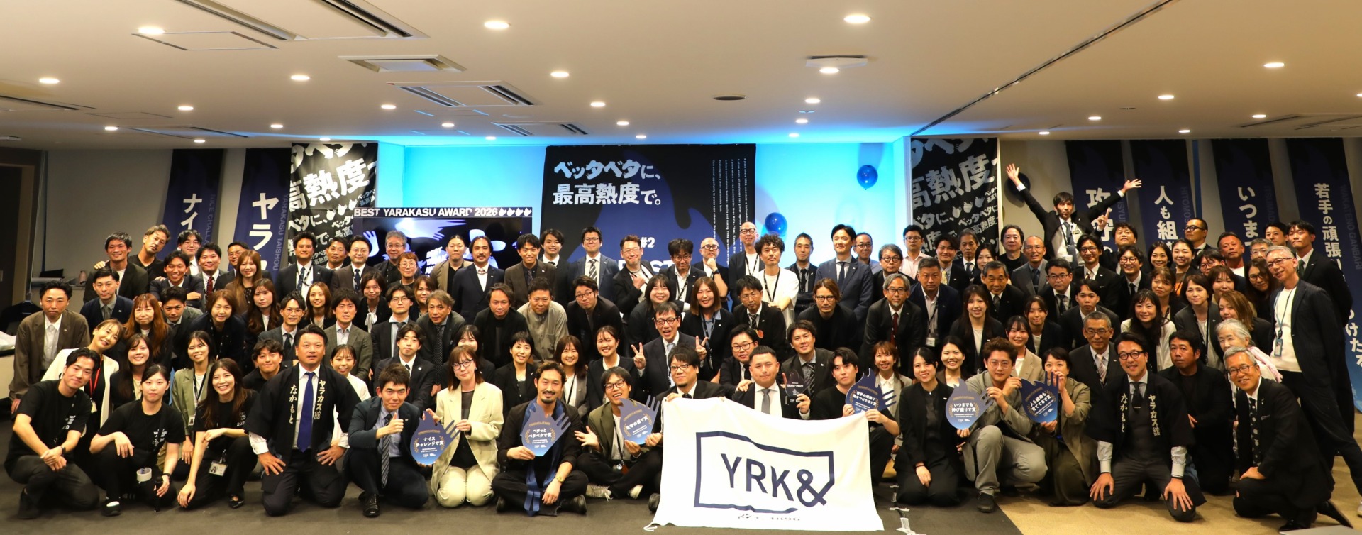 BEST YARAKASU AWARD 2026を終え、YRK＆の旗を持って集合する全社員の記念写真